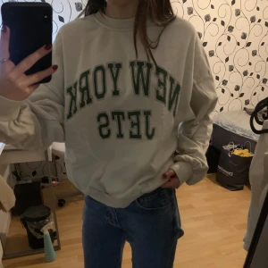 Beige sweatshirt med tryck - Säljer en beige sweatshirt från H&M med texten 'New York Jets' i grönt på framsidan. Tröjan har långa ärmar och en rund halsringning. Perfekt för en avslappnad stil.