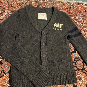 Aberchrombie & Fitch grå kofta - Säljer denna sjukt snygga kofta från Aberchrombie & fitch! Den är storlek M och kan nog passa mindre. 