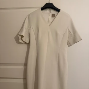 Beige klänning från BOSS - Elegant beige klänning från BOSS med v-ringning och korta ärmar. Perfekt för en stilren look. Klänningen har en figursydd passform som framhäver silhuetten.