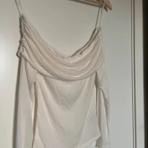 Vit långärmad topp med draperad hals - Säljer en elegant vit långärmad off-shoulder topp. . Perfekt för en stilren look. Toppen är i en mjuk och bekväm kvalitet.