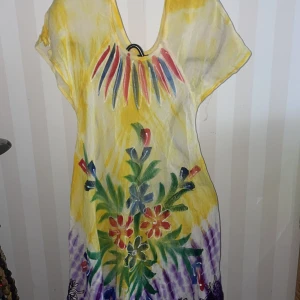 Färgglad klänning i rayon st. S/M - Säljer en färgglad klänning i 100% rayon med ett livfullt blommönster. Klänningen har en v-ringad hals och korta ärmar. Den domineras av gula och lila toner med inslag av grönt och rött. Perfekt för en somrig look!