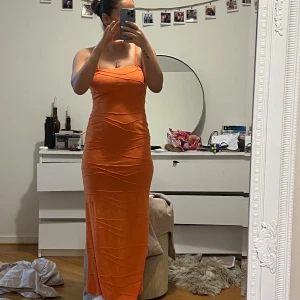Orange långklänning med smala axelband - Snygg orange långklänning med smala axelband och en figurnära passform. Perfekt för sommarens festligheter. Klänningen har en enkel och stilren design som framhäver figuren.