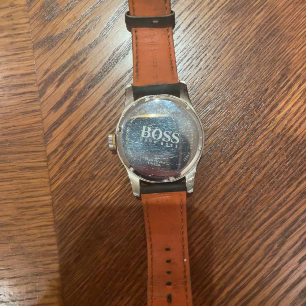 Snygg klocka från Boss Orange med svart urtavla och orange detaljer. Klockan har en svart läderrem med vita sömmar och ett robust silverfärgat boett. Perfekt för den som vill ha en stilren och modern accessoar. Water resistent 3 ATM / up to 30m. All steinless steel.. Asusteet.