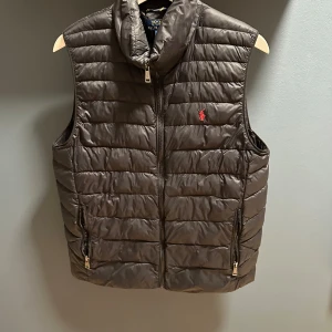 Polo Ralph Lauren väst - Snygg svart dunväst från Polo Ralph Lauren med dragkedja och broderad logotyp på bröstet. Västen har två fickor med dragkedja framtill. Använd några gånger men i fint skick, lite defekter på ena fickan (se sista bilden) Storlek 18-20, skulle säga att den passar både s och m 