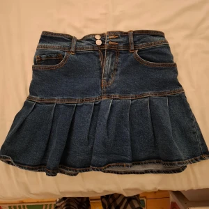 Jeanskjol från Wild Fable - Snygg jeanskjol från Wild Fable med volangdetaljer och två knappar framtill. Kjolen har en klassisk blå denimfärg och är perfekt för en avslappnad stil. Den har också praktiska fickor och bälteshällor.