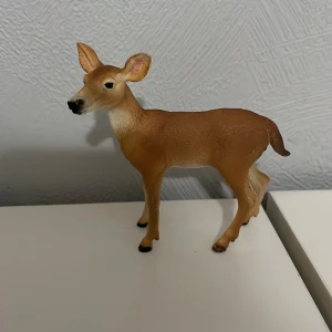 Schleich rådjur - En liten och detaljerad hjortfigur i plast. Figuren har en naturlig brun färg med ljusare detaljer på magen och svarta hovar. Perfekt för samlingar eller som dekoration.