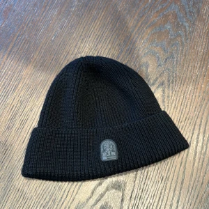 Svart stickad mössa från Parajumpers - Snygg svart stickad mössa från Parajumpers med ribbad design. Perfekt för att hålla värmen under kyliga dagar. Diskret logga framtill ger en stilren look. 1299kr nypris