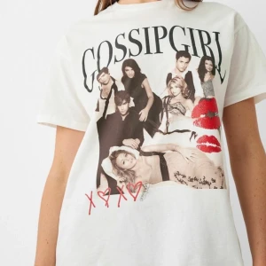 Vit Gossip Girl t-shirt - Cool vit t-shirt med Gossip Girl-tryck. Designen har ett stort tryck av karaktärerna från serien och röda läppavtryck. Perfekt för fans av serien som vill ha en stilren och trendig look.
