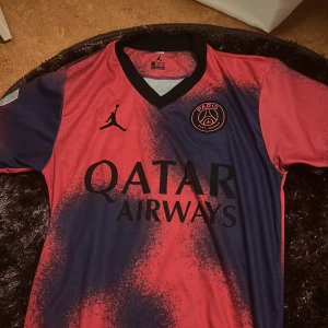PSG fotbollströja - Snygg PSG fotbollströja i röd och blå färg med korta ärmar. Tröjan har Paris Saint-Germain-loggan på bröstet och Messi 10 på ryggen. Perfekt för fans av både PSG och Messi!