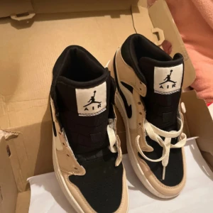 Nike Air Jordans i beige och svart - Säljer ett par Nike Air Jordans i beige och svart. Skorna har en klassisk design med snörning och den ikoniska Air Jordan-loggan på sidan. Perfekta för dig som älskar stil och komfort i ett.