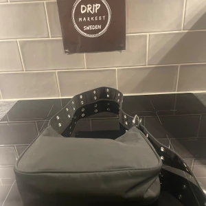 Svart Damväska från Weekday - En helt ny och oanvänd Snygg svart damväska från Weekday med coola nitar på axelremmen. Väskan har en praktisk dragkedja för säker förvaring. Perfekt för att ge din outfit en edgy touch.