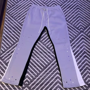 Grå mjukisbyxor med vita detaljer - Snygga grå mjukisbyxor med vita sidopaneler och stänkmönster i olika färger. Byxorna har en dragsko i midjan för justerbar passform och är perfekta för en avslappnad stil.