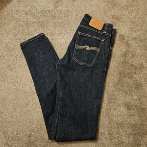 Mörkblå jeans från Nudie Jeans - Snygga mörkblå jeans från Nudie Jeans med klassisk femficksdesign och kontrastsömmar. Perfekta för en stilren look. Jeansen har en normal passform och är tillverkade i högkvalitativt denim.