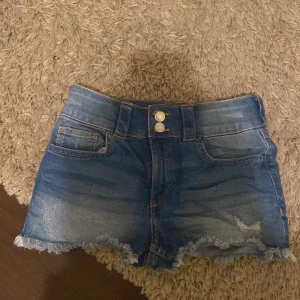 Blå jeansshorts från H&M - Säljer ett par snygga blå jeansshorts från H&M. De har en fransig kant och klassisk femficksdesign med knapp och dragkedja framtill. Perfekta för en avslappnad stil.