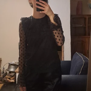 Svart prickig blus med volangdetalj - Snygg svart blus med prickigt mönster och volangdetalj framtill. Blusen har långa ärmar i transparent material. Storleken är 170 men skulle endå säga xs/s jag själv har båda xs/s och den passar bra! Köpte den för några år sedan använt ett par gånger bara 