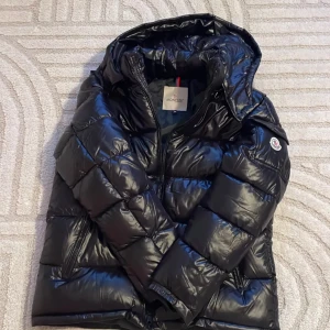 Svart dunjacka från Moncler - Säljer en snygg svart dunjacka från Moncler med glansig finish. Jackan har en huva och dragkedja framtill. Perfekt för kyliga dagar och håller dig varm och stilren nfc Scan funkar också.