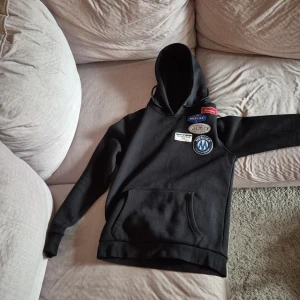 Svart hoodie från Product of Mercier - Snygg svart hoodie från Product of Mercier med flera märken på framsidan. Den har en klassisk känguruficka och en bekväm huva. Perfekt för en casual look.