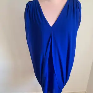Snygg blå klänning med v-ringning och öppen rygg. Den har en draperad design som ger en elegant look. Perfekt för en kväll ute eller en speciell tillställning.