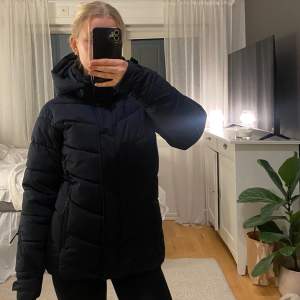 Säljer en svart dunjacka/ skidjacka med huva. Jackan har en pufferdesign och dragkedja framtill. Den är köpt förra året och endast använd 3 dagar då jag har en annan jacka. Den är i strl 170 barn, men den passar perfekt på mig som brukar ha Xs. Den är bra vindtät och har ett snölås. Den har också en ficka på armen för liftkort. HÖR AV DIG OM DU ÄR INTRESSERAD ELLER OM DU VILL DISKUTERA PRISET!🥰🥰