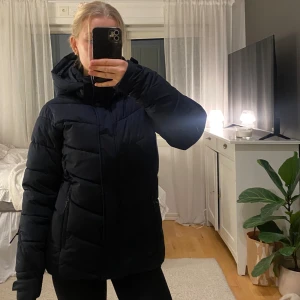 Svart skidjacka från Intersport  - Säljer en svart dunjacka/ skidjacka med huva. Jackan har en pufferdesign och dragkedja framtill. Den är köpt förra året och endast använd 3 dagar då jag har en annan jacka. Den är i strl 170 barn, men den passar perfekt på mig som brukar ha Xs. Den är bra vindtät och har ett snölås. Den har också en ficka på armen för liftkort. HÖR AV DIG OM DU ÄR INTRESSERAD ELLER OM DU VILL DISKUTERA PRISET!🥰🥰