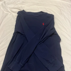 Mörkblå tröja från Ralph Lauren - Säljer en stilren mörkblå tröja från Ralph Lauren med det klassiska röda logotypen på bröstet. Tröjan har långa ärmar och en rund halsringning. Perfekt för en avslappnad och snygg look.