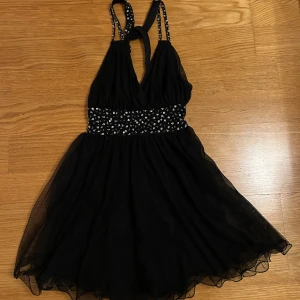 Svart klänning från Model Behaviour - Säljer en sååå fin svart klänning från Model Behaviour med glittriga detaljer och öppen rygg. Klänningen har en kort längd och är ärmlös med smala axelband. 🖤🫶🏻🙏🏻