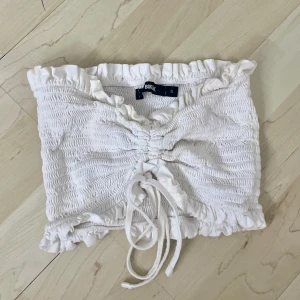 Vit topp  - En vit topp med strechigt ribbat material. Endast använd få gånger tidigare. Har snören för att anpassa storleken till önskad passform. Passar perfekt med en kjol och en blazer över🌺