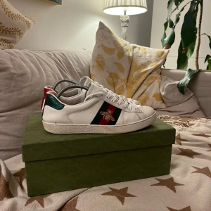 Gucci Ace Bee - Snygga vita sneakers från märket Gucci med en broderad bi-detalj på sidan. Skorna har en unik design med röd och grön häl i ormskinnsmönster. Allt Og följer vilket inkluderar låda, dustbags och skosnören.   Skorna är i bra skick men finns tecken på användning vid insidan och lite vid utsidan. Storlek 43  Skriv vid vidare funderingar!