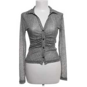 Svartvit prickig skjorta från Stradivarius - Snygg svartvit prickig skjorta från Stradivarius med långa ärmar och knappar framtill. Perfekt för en stilren look med en touch av retro. Tillverkad i ett lätt och bekvämt material.