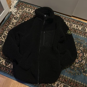 Svart teddyjacka från Stone Island - Säljer en svart teddyjacka från Stone Island med dragkedja och hög krage. Jackan har en broderad logotyp på ärmen och en praktisk bröstficka med dragkedja. Perfekt för kyliga dagar! Kom med offer fick i julklapp av min storebror pris prutbart öppen till byten!!!!
