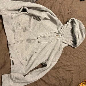 Grå hoodie med dragkedja - Säljer en bekväm grå hoodie med dragkedja och justerbar huva. Perfekt för en avslappnad stil. Den har praktiska fickor framtill och långa ärmar.💕