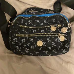 Svart axelväska från Giulia Pieralli - Snygg svart axelväska från Giulia Pieralli med vita mönster och guldfärgade dragkedjor. Väskan har flera fack och justerbar axelrem. Perfekt för att hålla ordning på dina saker med stil.