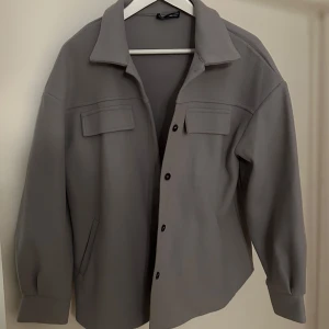 Grå jacka från Shein - Snygg grå jacka från Shein med knappar framtill och två bröstfickor. Jackan har en klassisk krage och långa ärmar, perfekt för en stilren look. Tyget är i fleece och är inte så tjockt men håller ändå värmen mycket bra. 