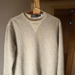 Grå sweatshirt från Polo Ralph Lauren - Ny pris 2600 Säljer en stilren grå sweatshirt från Polo Ralph Lauren. Tröjan har en klassisk rund halsringning och ribbade muddar vid ärmslut och nederkant. Perfekt för en avslappnad look.