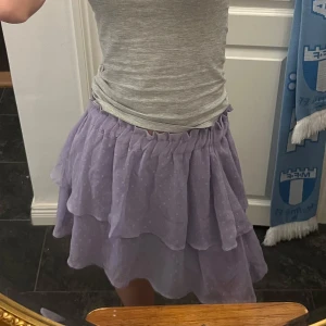 Lila volangkjol - Charmig lila kjol med volanger och prickigt mönster. Perfekt för sommaren! Kjolen har en elastisk midja för bekväm passform och är dessutom perfekt längd då den inte ät för kort så man visar allt