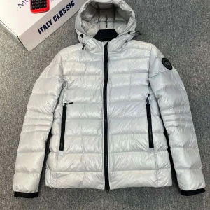 Vit dunjacka från Canada Goose - Snygg och varm vit dunjacka från Canada Goose med huva och svarta dragkedjor. Jackan har en klassisk pufferdesign och är perfekt för kyliga dagar. Märkeslogga på ärmen ger en exklusiv touch.