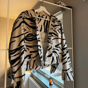 Zebramönstrad jacka - Snygg zebramönstrad jacka i svart och beige. Jackan har en croppad design med knappar framtill och långa ärmar. Perfekt för att ge din outfit en cool touch.