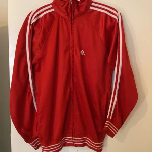 Röd träningsjacka från Adidas - Träningsjacka/ziphoodie från Adidas. Jackan har dragkedja och hög krage, perfekt för sport. Använd fåtal gånger, Stl S-M