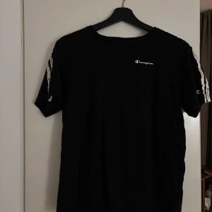 Svart t-shirt från Champion - Säljer en svart t-shirt från Champion med korta ärmar och logotyp på bröstet. Perfekt för en avslappnad stil.