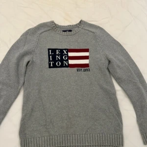 Grå tröja från Lexington - Säljer en stilren grå tröja från Lexington med ett broderat märke på bröstet i blått, rött och vitt. Tröjan har långa ärmar och ribbade kanter vid hals, ärmslut och nederkant. Perfekt för en avslappnad och klassisk look.