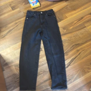 Svarta jeans från Gina Tricot - Snygga svarta jeans från Gina Tricot i storlek 140. Klassisk design med fem fickor och knappstängning. Perfekta för en stilren look.