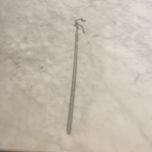 Silverfärgat halsband - Elegant och stilrent silverfärgat halsband med tunn kedja. Perfekt för att komplettera din look med en subtil touch av glans.