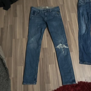 Replay anbass  - Säljer ett par snygga blå jeans från Replay med slitna detaljer och klassisk femficksdesign. De har en knappgylf och är tillverkade i ett slitstarkt denimtyg. Perfekta för en avslappnad stil.