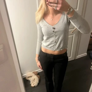 Grå långärmad topp med knappar - Säljer en stilren grå långärmad topp från oss Molly. Toppen har en v-ringning och knappar framtill, vilket ger en klassisk look. Perfekt för en avslappnad stil.