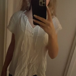 Vit blus från H&M - Säljer en söt vit blus från H&M med korta ärmar och knytband vid halsen. Blusen har små prickar och knappar framtill, vilket ger en romantisk touch. Perfekt för en avslappnad stil.