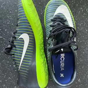 Nike Mercurial fotbollsskor - Snygga Nike Mercurial fotbollsskor i svart med gröna och blå ränder. Skorna har en vit Nike-logga och svart snörning. Perfekta för fotbollsplanen med sin greppvänliga sula.