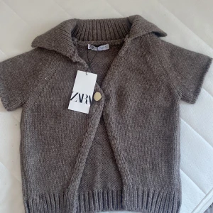 Beige stickad kofta från Zara - Säljer en snygg beige/brun stickad kofta från Zara med korta ärmar och en stor krage. Koftan har en enkel knapp framtill och ribbade detaljer vid ärmslut och nederkant. Perfekt för lager-på-lager-stil! Aldrig använd, säljer pågrund av att den inte passade🤍