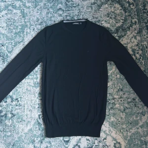 Svart J. Lindeberg 100% merinoull tröja - Säljer en stilren svart tröja från J.Lindeberg. Tröjan har en klassisk design med långa ärmar och ribbade muddar vid ärmslut och nederkant. Nästan nyskick, finns inga defekter. Storlek Small. Priset är ej hugget i sten!