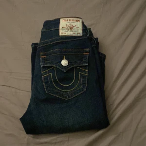 Mörkblå jeans från True Religion - Snygga mörkblå jeans från True Religion med ikonisk bakficka och kontrastsömmar. De har en klassisk femficksdesign och knappar med logotyp. Perfekta för en stilren look.  Säljer för dem tyvärr inte passade på mig💕