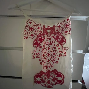 Vit och röd klänning från Kaleidoscope - Snygg vit klänning med röda detaljer från Kaleidoscope. Klänningen har ett unikt mönster och smala axelband, perfekt för sommarens varma dagar.